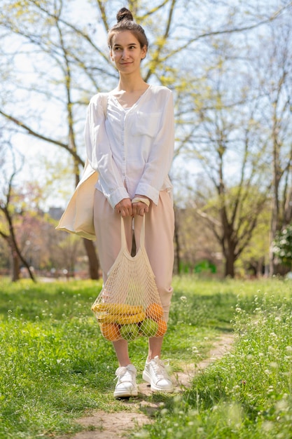 Full shot woman holding reusable bag with food in nature