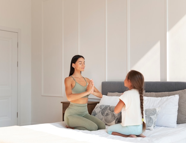 Полный снимок женщина и ребенок медитируют в постели