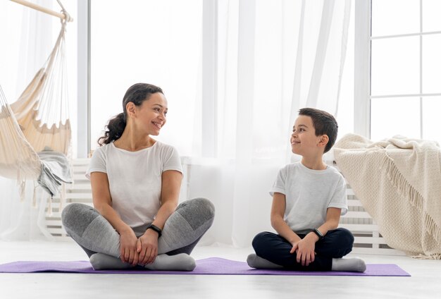 Full shot woman and kid sitting on mat