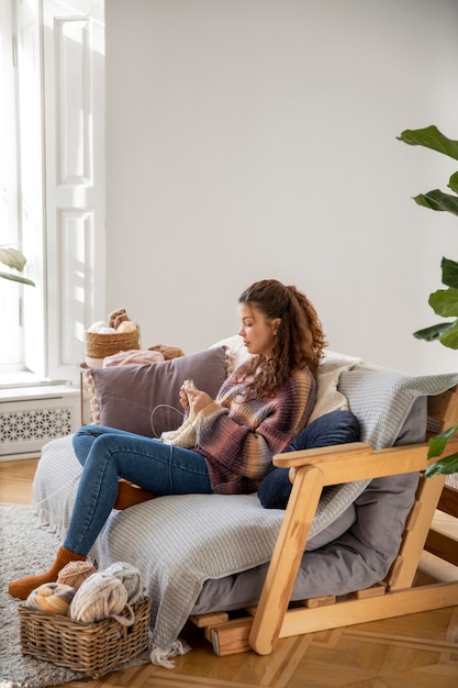 Foto gratuita donna del colpo pieno che lavora a maglia sul divano