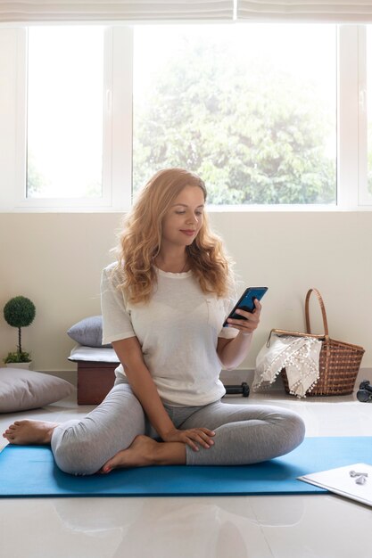 Full shot woman on mat with phone