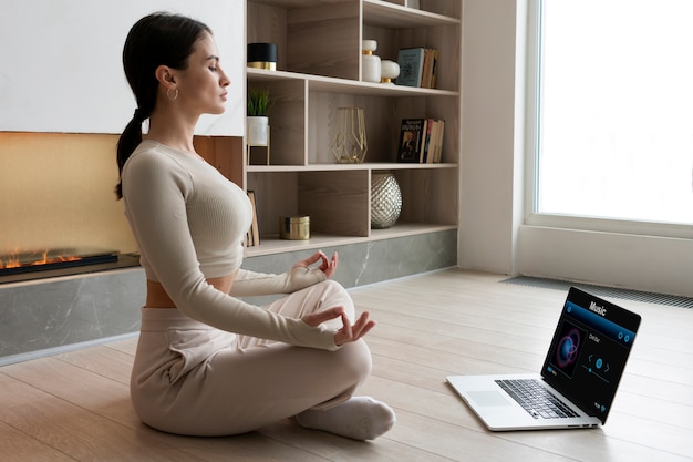 Free photo full shot woman meditating at home with laptop