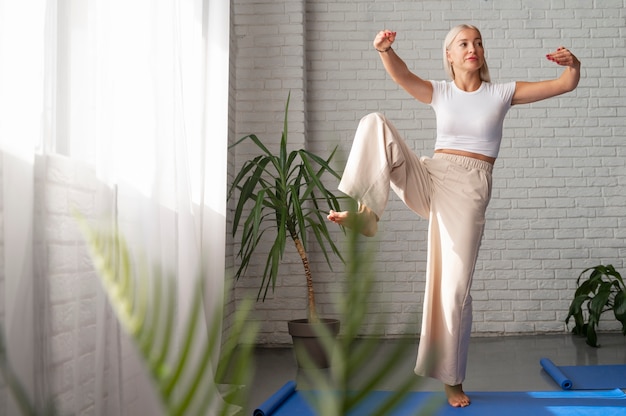 Foto gratuita donna del colpo pieno che pratica il tai chi all'interno