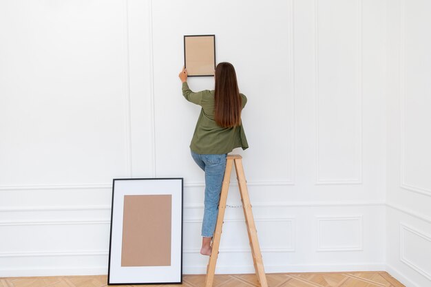 Full shot woman putting frame on wall