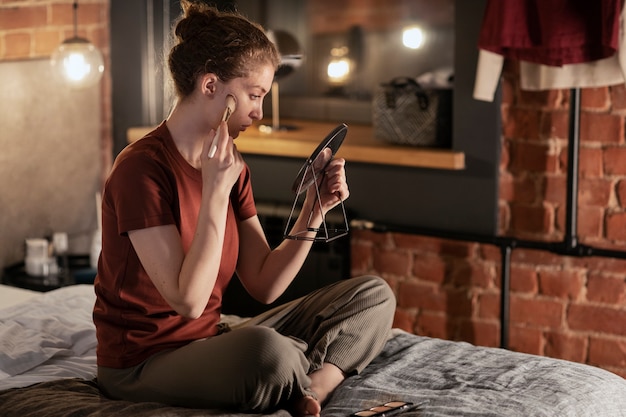 Full shot woman putting on makeup in bedroom