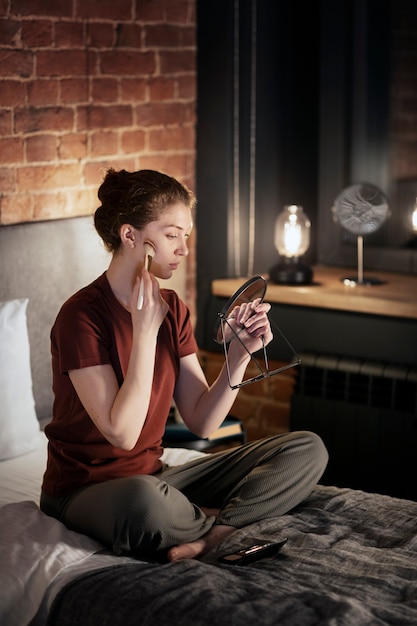 Full shot woman putting on makeup in bedroom