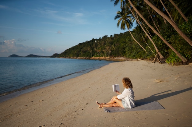 Free photo full shot woman reading on beach