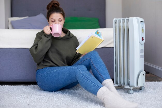 Full shot woman reading book near heater