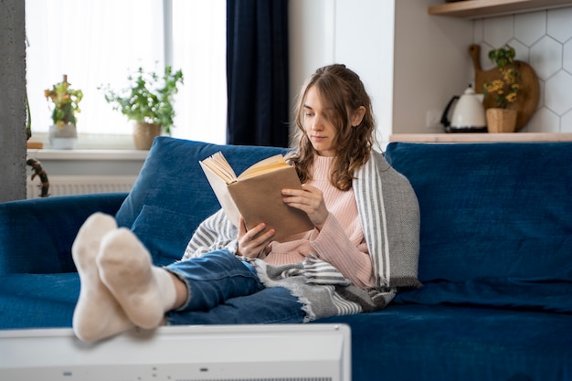 Женщина в полный рост читает дома возле обогревателя
