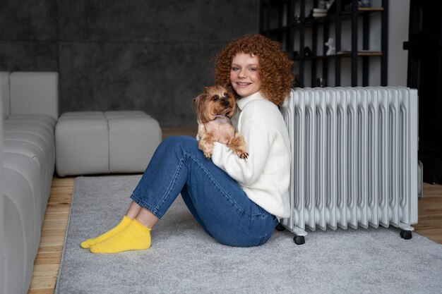 Full shot woman sitting near heater with dog