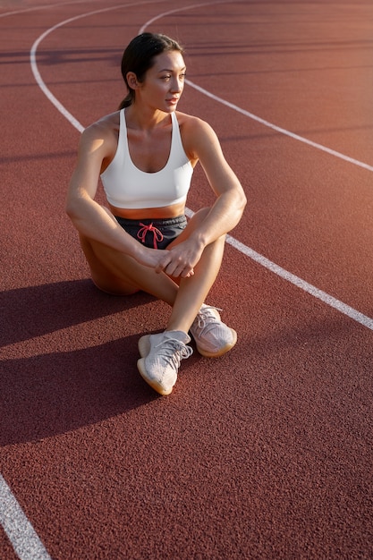 Foto gratuita donna del colpo pieno che si siede sulla pista da corsa