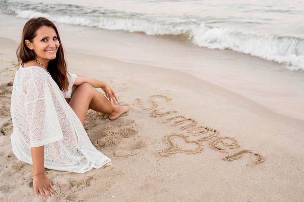 Foto gratuita donna piena del colpo che si siede sulla sabbia