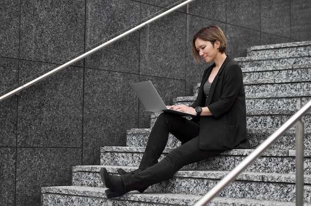 Free photo full shot woman on stairs with laptop