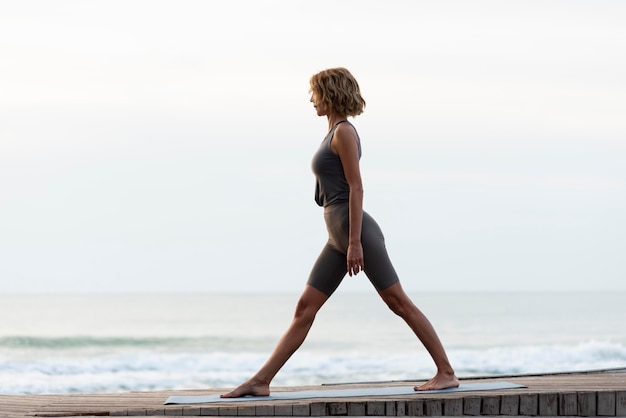 Free photo full shot woman standing on yoga mat outside