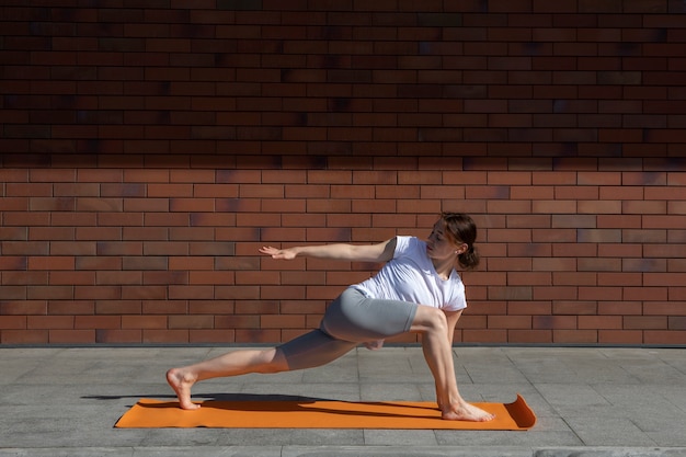 Foto gratuita donna della foto a figura intera che allunga sulla stuoia di yoga