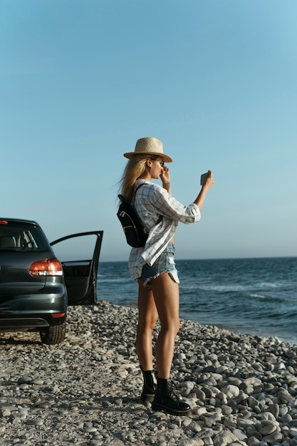 Free photo full shot woman taking photos of sea by car