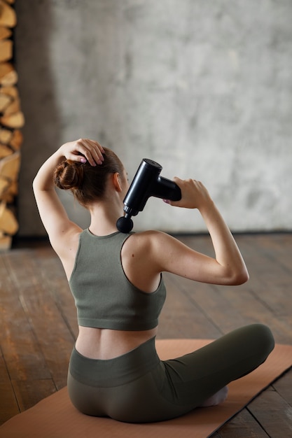 Full shot woman using massage gun on neck