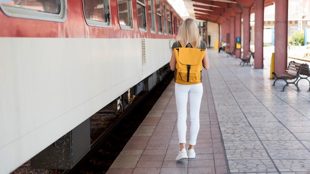 Full shot woman with backpack walking along train