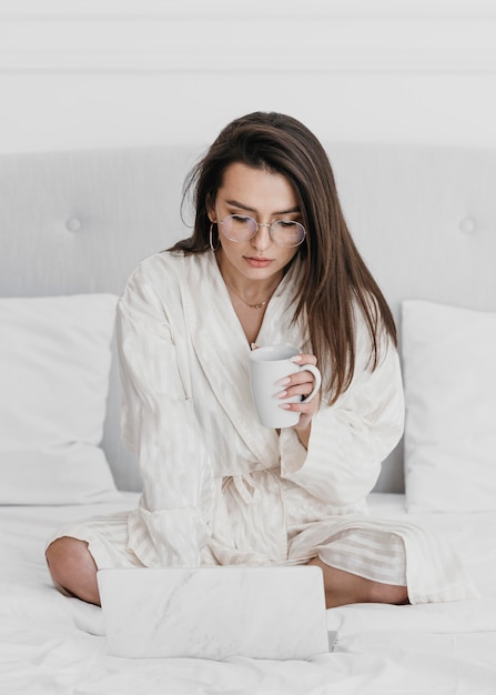 Donna piena del colpo con la tazza ed il computer portatile