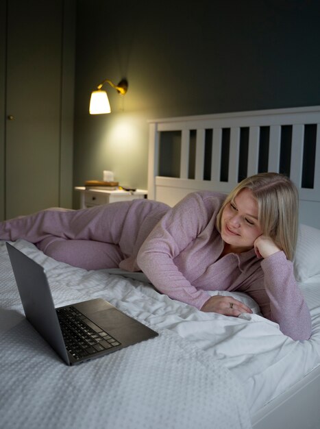 ベッドでノートパソコンを持つフルショット女性