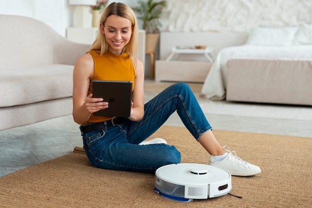 Free photo full shot woman with robotic vacuum cleaner at home