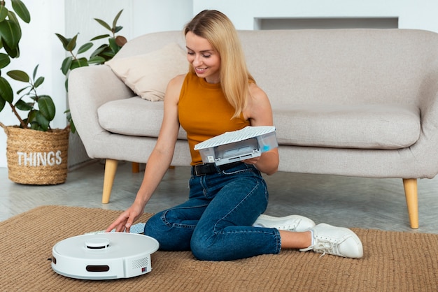 Foto gratuita donna a figura intera con aspirapolvere robotico a casa