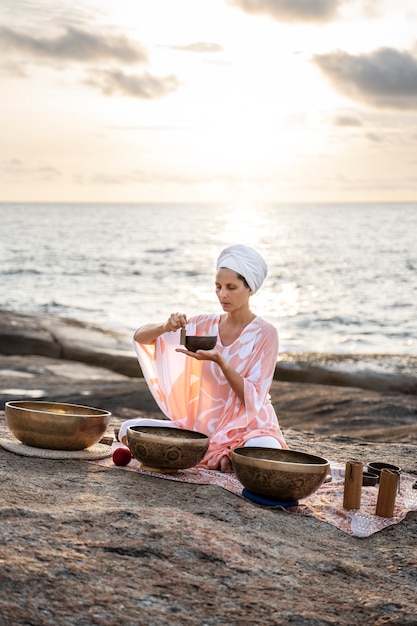 Бесплатное фото Женщина в полный рост с поющими чашами на берегу моря