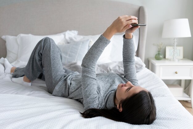 Full shot woman with smartphone in bed