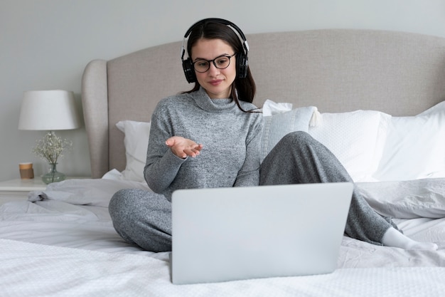 Full shot woman working with laptop in bedroom