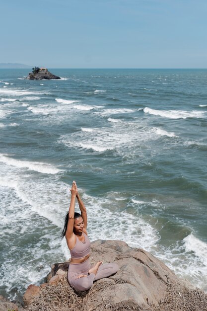 海辺でのフルショットの女性のヨガのポーズ