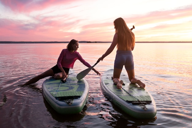 Free photo full shot women paddleboarding at sunset