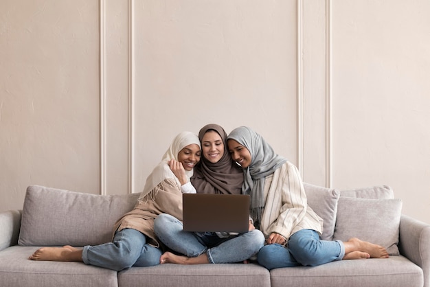 Free photo full shot women sitting on couch with device