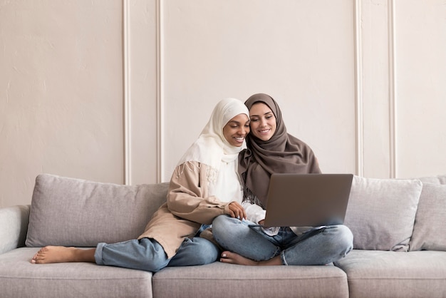 Full shot women sitting on couch with laptop