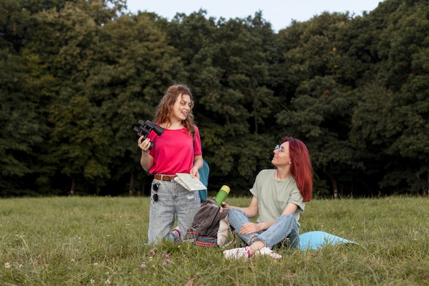 Foto gratuita donne del colpo pieno con il binocolo in piedi sull'erba e sorridente