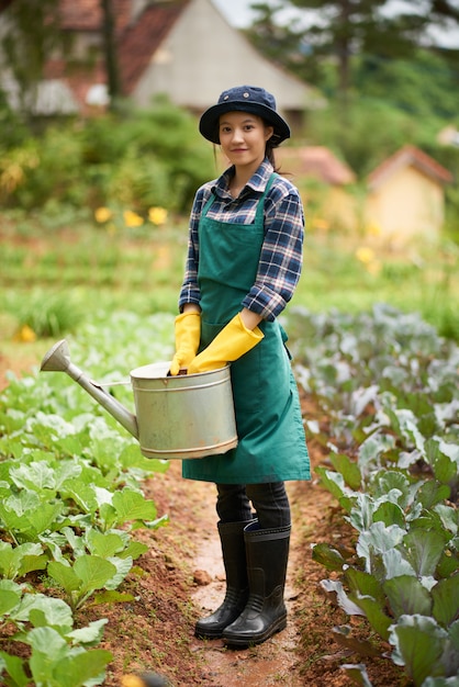 Full shot of young female gardener standing between plant beds with a funnel