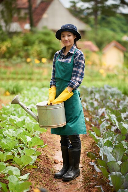 漏斗で植物のベッドの間に立っている若い女性庭師の完全なショット