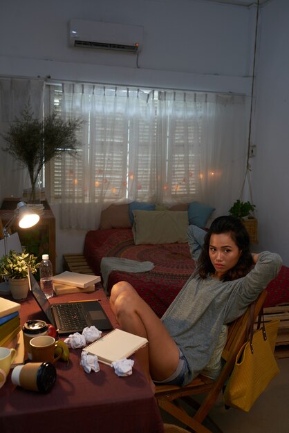 Full shot of young girl sitting in her room at the laptop with crumpled papers 