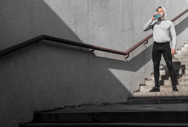 Full shot young man drinking water on stairs