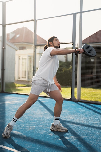 Полный снимок молодого человека, играющего в паддл-теннис