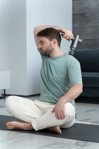 Full shot young man using massage gun