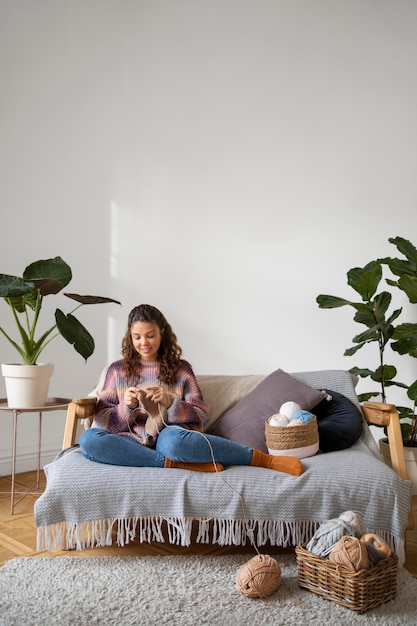 Full shot young woman knitting on couch