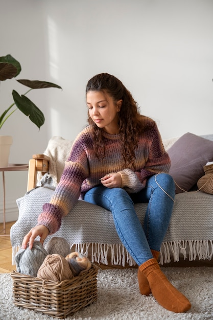 ソファで編み物のフルショットの若い女性
