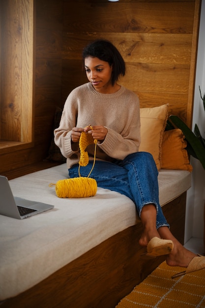 Free photo full shot young woman knitting at home