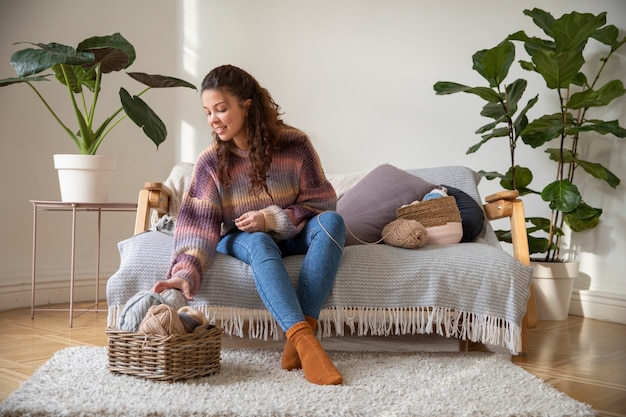 Full shot young woman knitting at home