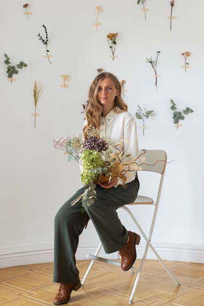 Full shot young woman sitting on chair with flowers