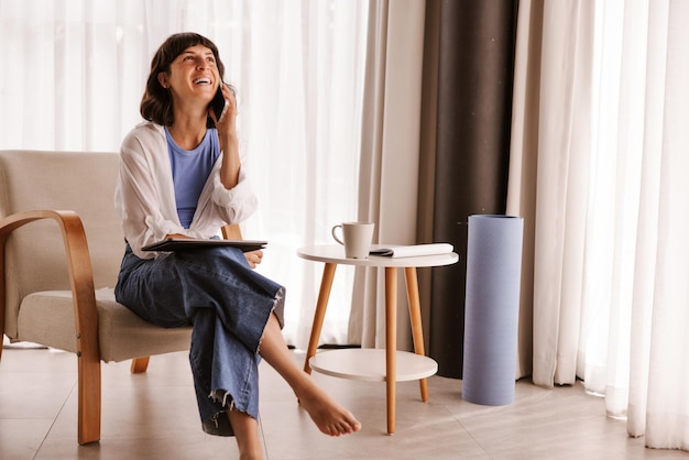 Full view of business woman sitting in chair in room luffing on phone