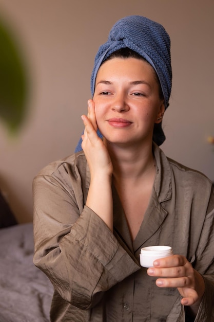 Full view of charming woman with cream on face at home looking at mirror