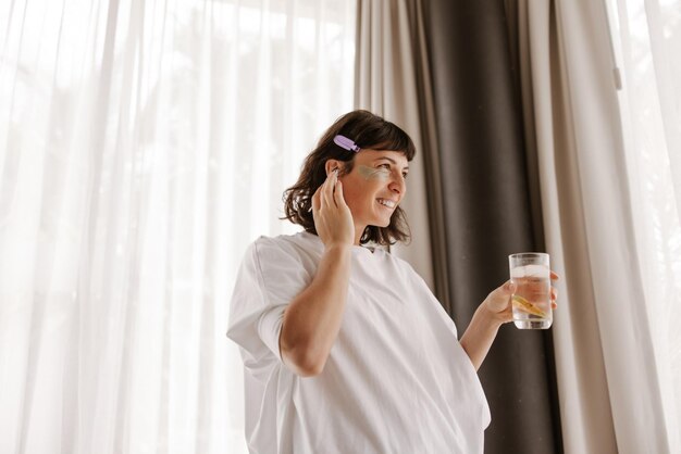 Full view of having fun woman with gel patches listening music with glass water