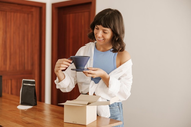 Foto gratuita punto di vista completo della donna sorridente che esamina l'attrezzatura del caffè a casa