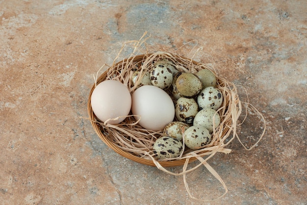 Полная плетеная корзина с перепелиными яйцами на мраморном столе.